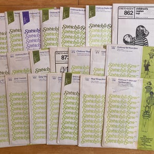 May include: A collection of vintage sewing patterns for children's clothing. The patterns are from the "Stretch & Sew" brand, featuring various designs like raglan tops and t-shirts. The covers are white with green and purple text and illustrations.