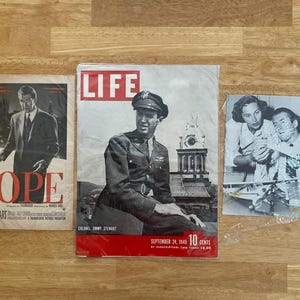 May include: Three vintage items are displayed: a movie poster for "Rope" starring James Stewart, a September 24, 1945, issue of "LIFE" magazine featuring Colonel Jimmy Stewart, and a black and white photograph. The magazine cover is red and white.