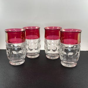 May include: Four vintage drinking glasses with a clear, textured base and a vibrant red top. The glasses have a silver rim and a decorative pattern. The glasses are arranged on a black surface.