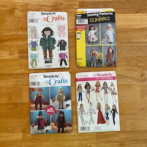 May include: Four Simplicity sewing pattern envelopes for doll clothes. The collection includes patterns 5733, 7069, 5676, and 4702, featuring illustrations of various outfits for 18-inch and 11.5-inch dolls, including jackets, pants, dresses, and skirts.