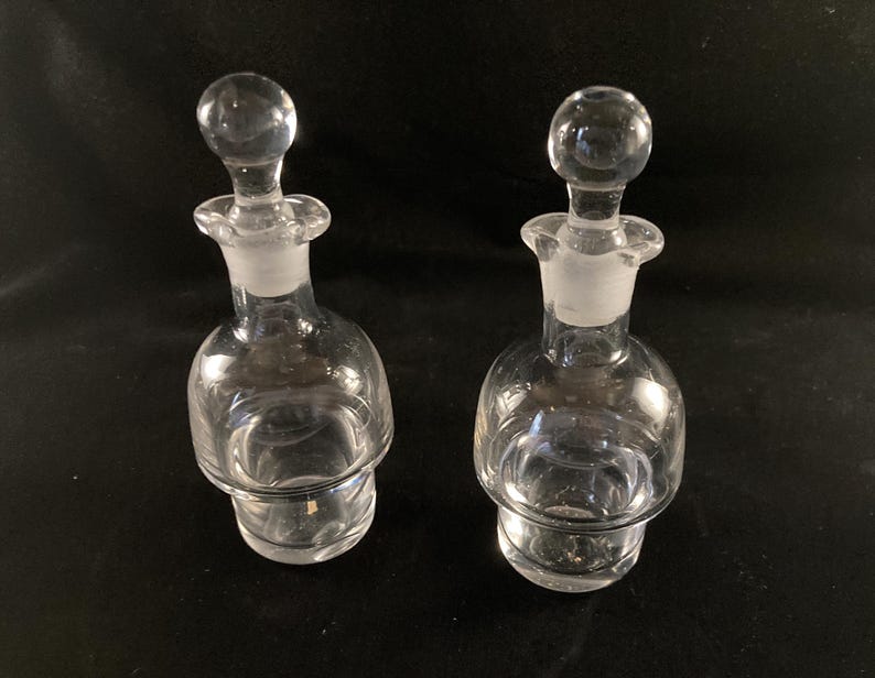 May include: Two clear glass bottles with stoppers. The bottles have a textured, rounded design and are perfect for holding oil or vinegar.