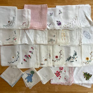 May include: A collection of square fabric handkerchiefs featuring various embroidered floral patterns, scalloped edges, and decorative stitching. The set includes white and pastel pink squares with colorful thread designs, including a blue clown figure.