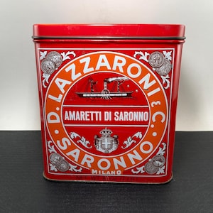 May include: A rectangular red tin with the words "D. LAZZARONI & C." and "AMARETTI DI SARONNO" in white and orange. The tin features a central circular design with a ship illustration and the word "MILANO". Decorative coin-like designs adorn the corners.