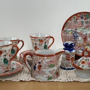 May include: A collection of antique Japanese porcelain tableware. The set includes cups, saucers, a creamer, a sugar bowl, a plate, and a salt and pepper shaker. The pieces are decorated with colorful scenes and figures.