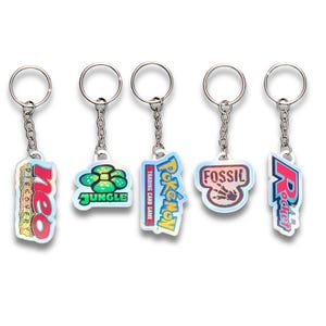 May include: Five keyrings with silver chains and rings. Each keyring features a different holographic design with text and logos, including "Neo Discovery", "Jungle", "Pokémon Trading Card Game", "Fossil", and "Rocket".