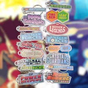 May include: A collection of colorful, rectangular and shaped keychains with various text designs. The keychains feature titles like "Ruby & Sapphire," "Emerald," "Hidden Legends," and "Crystal Guardians." Each keychain has a silver keyring.