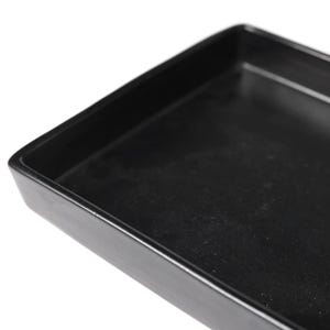 Puede incluir: Primer plano de una bandeja rectangular negra con bordes ligeramente elevados. La bandeja tiene un acabado mate y parece estar hecha de un material sólido. Las esquinas son redondeadas y el diseño es simple y funcional.