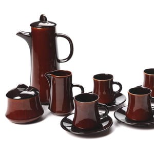 May include: A complete coffee set in a rich brown glaze. The set includes a tall coffee pot, a creamer, a sugar bowl with a lid, and six cups with saucers. The cups have a rounded shape and a dark brown interior.
