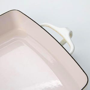 May include: A rectangular baking dish with a light pink interior and a black rim. The dish has white handles and is set against a white background. This enamelware dish is ideal for baking and serving.
