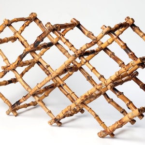 May include: A collapsible wine rack constructed from natural bamboo stalks. The structure features a crisscross lattice design with multiple diamond-shaped openings for bottle storage, showcasing the organic tan and dark brown textures of bamboo.