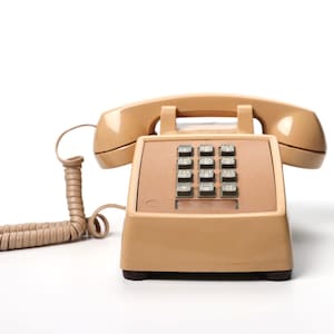 May include: A beige landline telephone with a push-button keypad featuring black keys with white numbers and letters. The device includes a matching handset resting on the base and a coiled cord connecting the handset to the main unit.