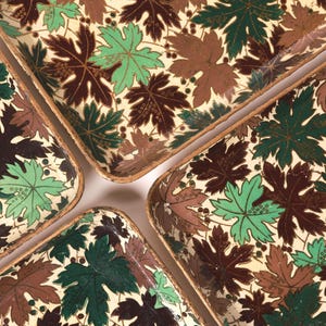 May include: Four rectangular trays with a leaf pattern in shades of green, brown, and cream. The trays have a light brown border and are arranged to show their corners. The leaf design is detailed and covers the entire surface.