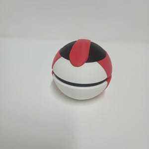 May include: A spherical object with a segmented design. The top section is black with a red stripe, while the lower half is white. The object appears to be a decorative or functional item.