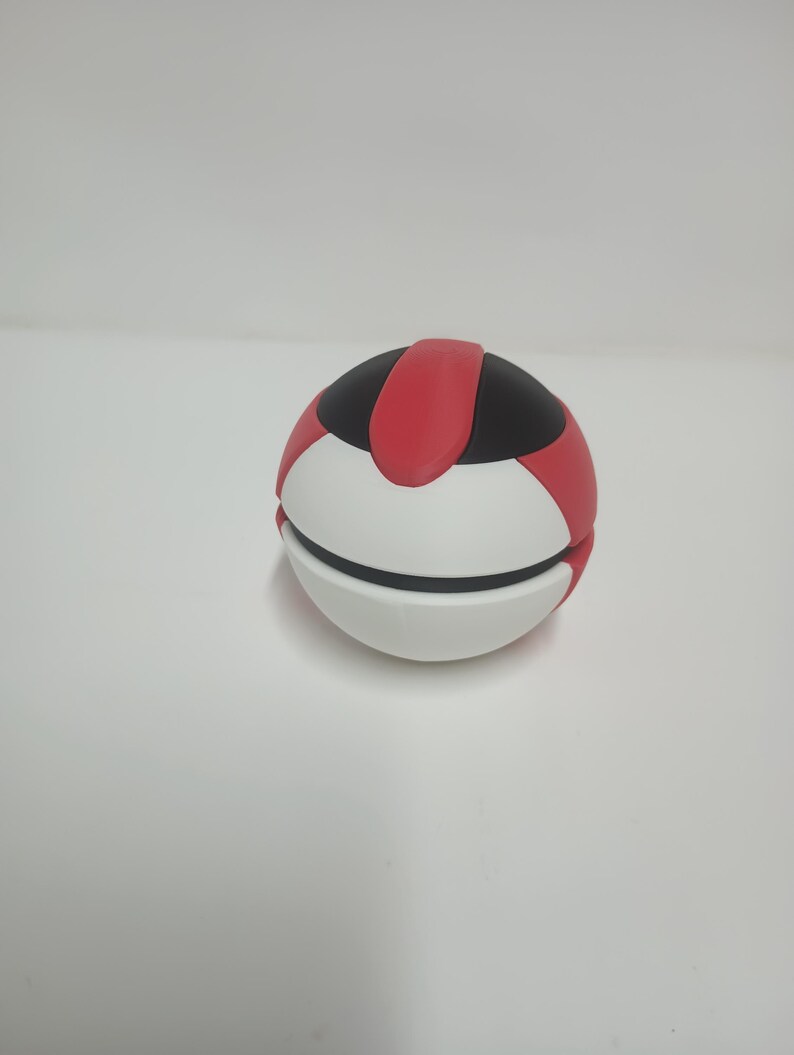 May include: A spherical object with a segmented design. The top section is black with a red stripe, while the lower half is white. The object appears to be a decorative or functional item.