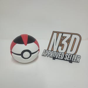 May include: A white, red, and black ball with a circular design, resembling a cartoon character's ball. Next to it is a black and orange sign that reads "N3D APPROVED SELLER".