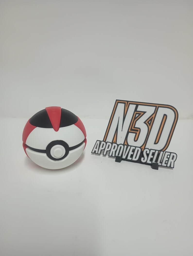 May include: A white, red, and black ball with a circular design, resembling a cartoon character's ball. Next to it is a black and orange sign that reads "N3D APPROVED SELLER".