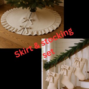 Puede incluir: Una falda de árbol de Navidad beige con borde con volantes y dos lazos. Tres medias beige a juego con lazos cuelgan de una escalera. Un árbol de Navidad está en el fondo.