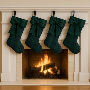 Puede incluir: Cuatro calcetines navideños con lazos verdes y un estampado de cuadros cuelgan sobre una chimenea con fuego. Los calcetines son verdes y azul marino. La chimenea es blanca con un interior de ladrillo.