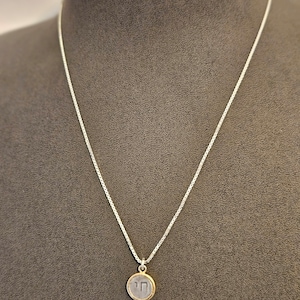 May include: A silver chain necklace with a round pendant featuring the Hebrew letter 'Chai' in silver with a gold border.