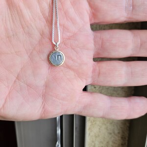 May include: A silver chain necklace with a small round pendant. The pendant is silver with a gold rim and has the Hebrew letter "Chai" inscribed on it.