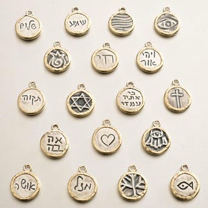 May include: A collection of 16 gold-toned metal charms with various designs and Hebrew lettering. The charms are round and have a textured surface. Some of the designs include a Star of David, a cross, a heart, and a fish.