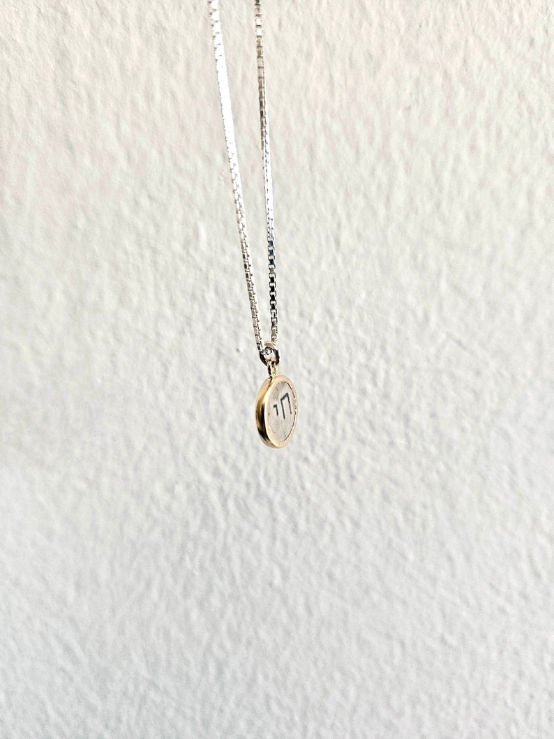 May include: A silver chain necklace with a small gold pendant featuring the Hebrew letter 'Chai' inscribed in black.