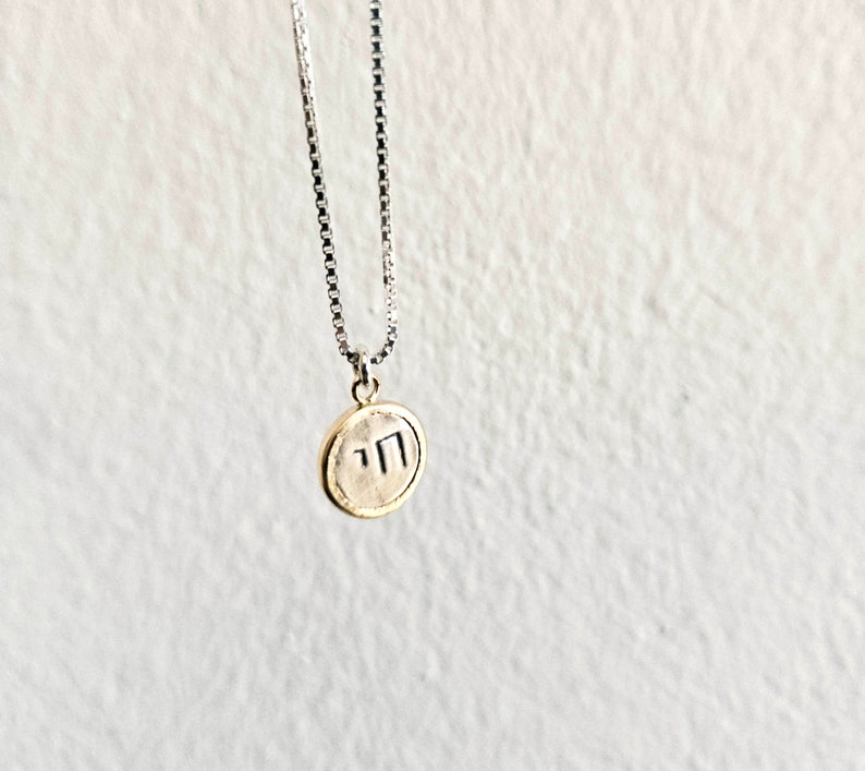 May include: A silver chain necklace with a round gold pendant featuring the Hebrew letters "nun" and "yud" in black.