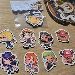 Op de afbeelding: Een verzameling kleurrijke stickers met personages uit de anime-serie One Piece. De stickers tonen verschillende personages in chibi-stijl, met een pakje stickers in een plastic hoesje met de tekst "Pack Pegatinas".