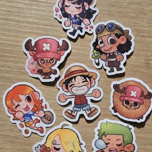 Op de afbeelding: Een verzameling kleurrijke stickers in cartoonstijl met personages uit de anime-serie One Piece. De stickers tonen verschillende personages in dynamische poses, met levendige kleuren en gedetailleerde ontwerpen. De stickers liggen op een lichtbruin oppervlak.