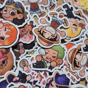 Op de afbeelding: Een verzameling kleurrijke cartoonkarakterstickers. De stickers tonen verschillende personages met verschillende gezichtsuitdrukkingen en outfits. De stickers hebben een glitterafwerking en zijn waarschijnlijk voor decoratieve doeleinden.