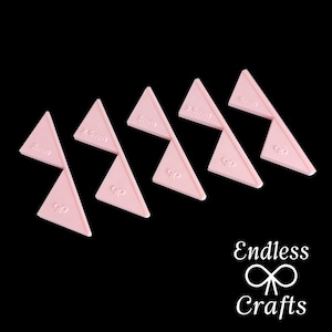 May include: Six pink plastic triangles with different measurements marked on them: 2mm, 2.5mm, 3mm, 3.5mm, 4mm, and 4.5mm. The triangles are arranged in a staggered pattern.