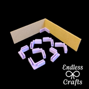 Könnte beinhalten: Ein Set mit 10 Eckschützern aus Kunststoff in Lavendelfarbe für Bastelarbeiten. Die Eckschützer sind aus Kunststoff und sollen Ecken vor Beschädigungen schützen. Die Eckschützer sind auf einem Stück Pappe abgebildet.