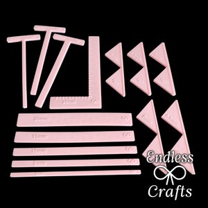 May include: Pink plastic tools for crafting and cake decorating. The set includes a ruler, a right angle, triangles, and straight edges in various sizes. The tools are labeled with measurements in millimeters.