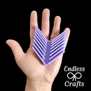 Könnte beinhalten: Eine violette Garn-Schale aus Kunststoff mit einem Chevron-Muster. Die Schale ist V-förmig und hat mehrere Schlitze zum Halten von Garn.
