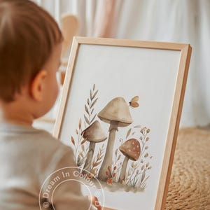 May include: A framed watercolor print featuring three mushrooms in shades of brown and beige, with a small butterfly and foliage. The artwork is in a light wooden frame. The text "Dream In Colour" is visible on the bottom of the print.