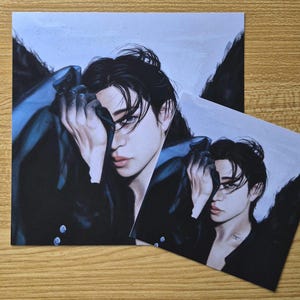 May include: Two art prints featuring a portrait of a person with dark hair and a black outfit. The person's face is partially obscured by their hand. The prints have a blue and black color scheme.
