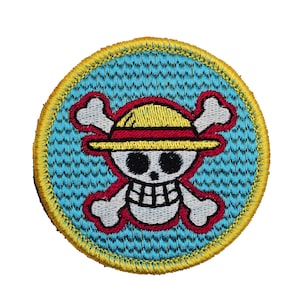 May include: A round, blue and yellow embroidered patch featuring a white skull wearing a yellow straw hat and crossed bones. The skull has black eyes and a red mouth.