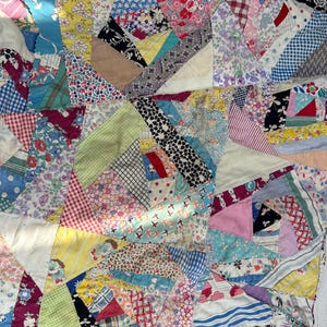 May include: A patchwork quilt with a variety of fabric patterns and colors. The quilt features geometric shapes and a mix of floral, striped, and solid fabrics in shades of blue, red, yellow, and green. The quilt is a handmade item.