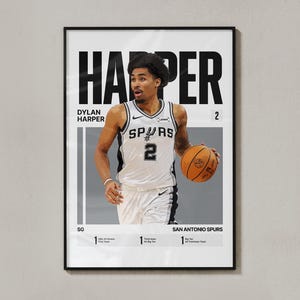 Könnte beinhalten: Ein gerahmtes Sportposter mit einer grafischen Illustration des Basketballspielers Dylan Harper in einem weißen San Antonio Spurs Trikot mit der Nummer 2. Der Text enthält seinen Namen, das Team, die Position SG und verschiedene Auszeichnungen.