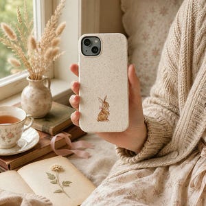 Woman holding bow bunny phone case next to tea and a window