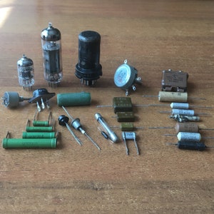 Puede incluir: Surtido de componentes electrónicos que incluyen tubos de vacío, resistencias, condensadores y un potenciómetro. Los componentes están dispuestos sobre una superficie de madera.