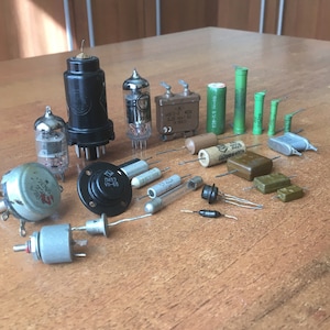 Puede incluir: Surtido de componentes electrónicos vintage, que incluyen tubos de vacío, condensadores, resistencias y transistores. Los componentes están dispuestos sobre una superficie de madera. Algunos de los componentes tienen marcas, como "MS711-3 400" y "2008".