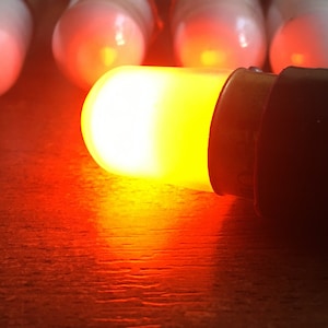 May include: A close-up of a single orange light bulb with a black base. The bulb is lit and casting a warm glow.
