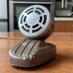 May include: Vintage brown and silver microphone with the text "MA-41 1960г." on the front. The microphone has a rounded head with a mesh grill and a brown base. The microphone is likely from the mid-20th century.