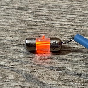 May include: A small, glowing orange light bulb with a silver base and a blue wire. The bulb is cylindrical and has a bright orange glow. The wire is twisted and connected to the bulb.