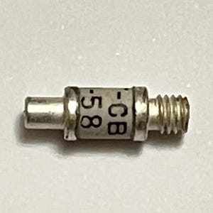 May include: A small, cylindrical metal component with a threaded end and a smooth, cylindrical extension. The component has the markings ".58 -CB" printed on its surface. The object is silver in colour.