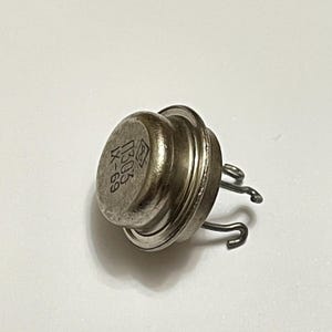 May include: A silver electronic component with three curved metal pins. The top of the component has the text "0303 IX-69" printed on it. The component has a circular, ridged design.