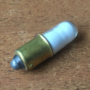 May include: A small, white, glass light bulb with a brass base and a silver tip.