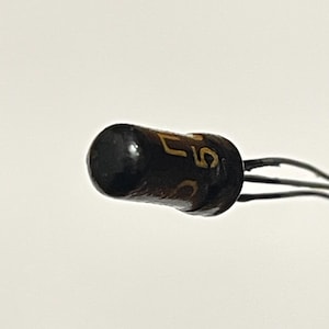 May include: A close-up of a small, dark brown electronic component with the text "57" in gold lettering. The component has three thin wires extending from one end. The background is plain white.