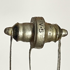 May include: Close-up of a vintage, silver-toned vacuum tube component. The tube has a cylindrical center section with the text "IV-5" printed on it. Thin wires extend from both ends of the tube, against a white background.